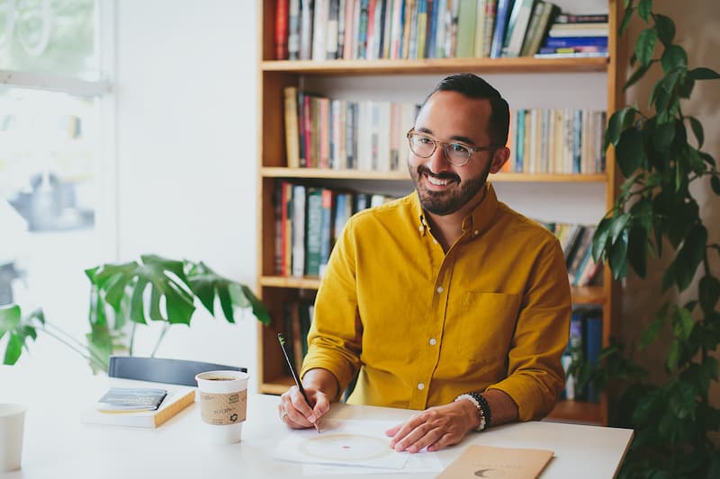 Dr. Cameron Martin smiling at his desk with a birth chart and bookshelf behind him